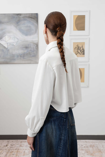 Close-up back left detail of white artisanal blouse — gathered sleeve and curved hem construction, nowhere studio