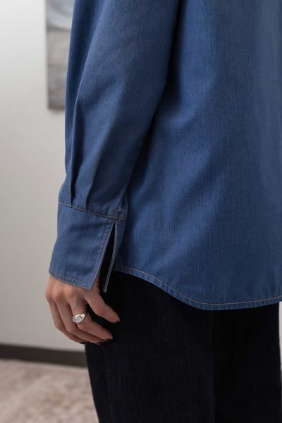 Close-up sleeve detail of denim utilitarian shirt — graphic topstitching as compositional accent, nowhere studio