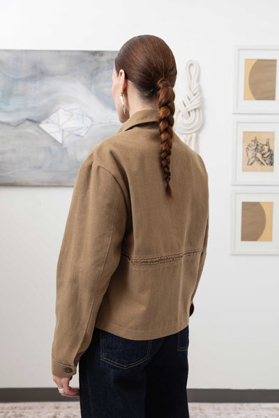 Close-up back left detail of workwear jacket in earth — selvedge fringe centre panel with reinforced seam construction, nowhere studio