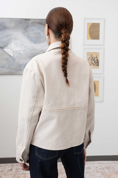 Close-up back left detail of workwear jacket in ivory — selvedge fringe panel and reinforced seam finish, nowhere studio