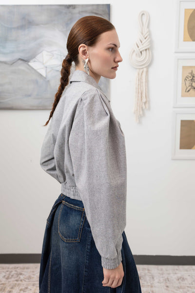 Close-up side detail of sculptural blouson jacket in granite — two-tone canvas texture with gathered waist seam, nowhere studio