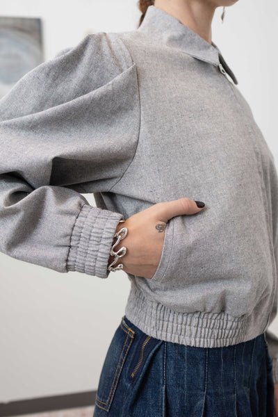 Side detail of sculptural blouson jacket in granite — pleated sleeve volume, welt pockets by nowhere studio