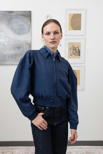 Close-up front view of sculptural blouson jacket in navy — metal zip closure and welt pocket detail in crinkled nylon, nowhere studio