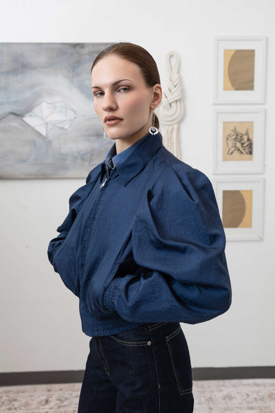 Close-up left side detail of sculptural blouson jacket in navy — pleated sleeve construction in water-resistant crinkled nylon, nowhere studio