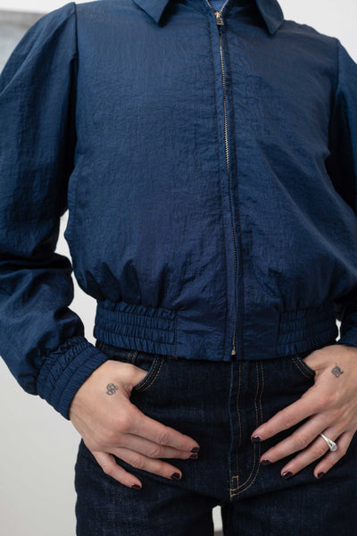 Front detail of sculptural blouson jacket in navy — welt pocket and zip hardware on water-resistant crinkled nylon, nowhere studio