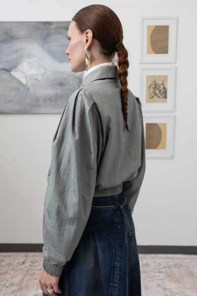 Close-up back left detail of sculptural blouson jacket in silver — elasticized hem and crinkled nylon construction, nowhere studio