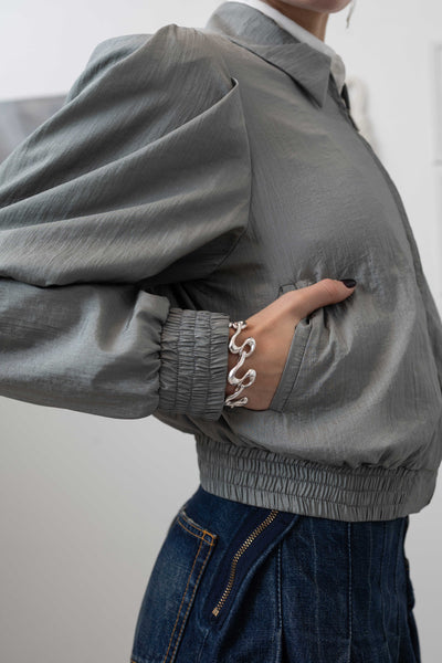 Front detail of sculptural blouson jacket in silver — metal zip closure and welt pocket in water-resistant crinkled nylon, nowhere studio